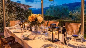 An outdoor dining table set with wine glasses, plates, and a candle centerpiece, surrounded by chairs and a pergola with a view of a mountainous landscape. - Villa Rocco, Traditional Luxury Near Town (Monsummano)