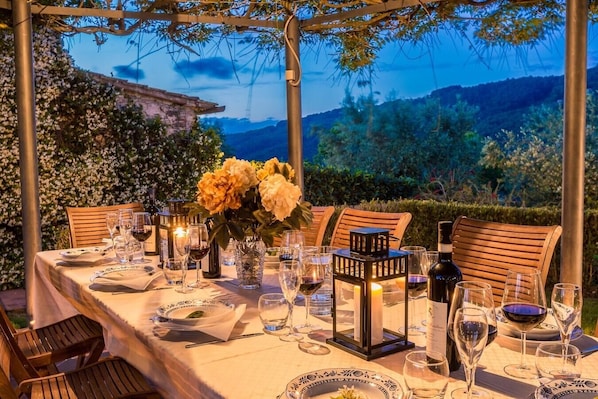 An outdoor dining setup with a table set for a meal, surrounded by chairs, and a view of a mountainous landscape.