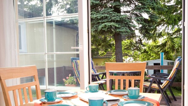 An outdoor dining area with a table set for four, chairs, and a view of a house and trees. - Vacation cottage Rohde, Germany (Binz)