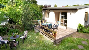 A patio area with a table and chairs, surrounded by a garden and a white building with a window. - Vacation cottage Rohde, Germany (Binz)