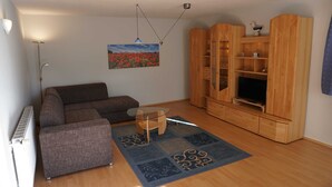 A living room with a sofa, a glass coffee table, a wooden entertainment unit with a TV, and a painting on the wall. - Vacation cottage Rohde, Germany (Binz)