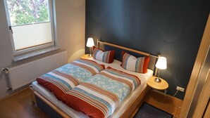 A bedroom with a bed, two bedside tables with lamps, a window with blinds, and a radiator. - Vacation cottage Rohde, Germany (Binz)