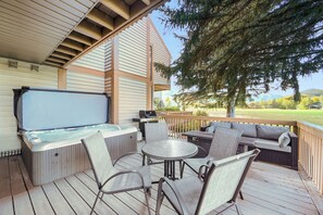Una terraza con hidromasaje, mobiliario exterior y vistas a un área verde.