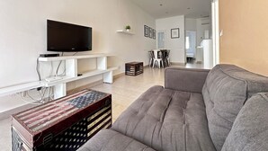 Ett modernt vardagsrum med en platt-TV, en grå soffa och en gammal resväska.