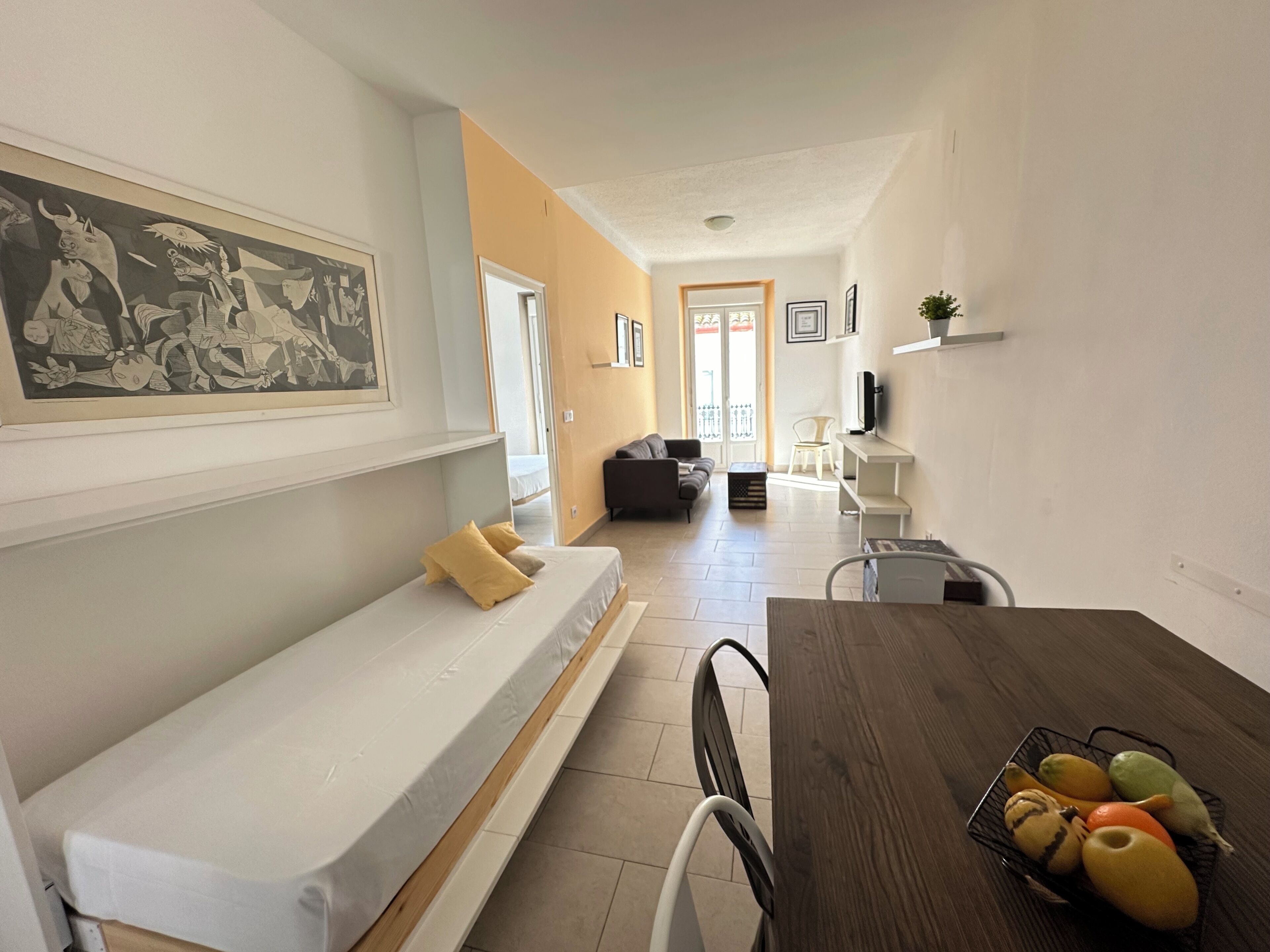 A modern living room with a sofa, a dining table with fruit, and a painting on the wall.