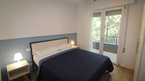 Een slaapkamer met een bed, een nachtkastje, een lamp en een schuifdeur naar een balkon.