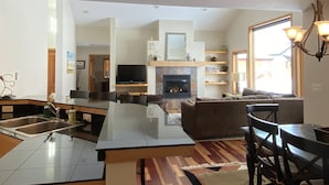 A spacious living area with a fireplace, a dining table, and a kitchen with a sink. - Cozy Home on the Idaho side of the Teton mountains- AC and a View! (Driggs)