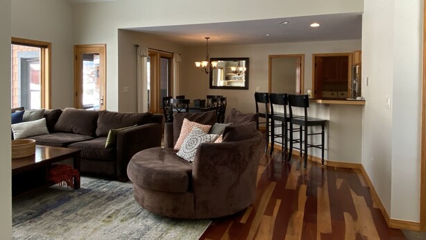 A spacious living room with a large brown sofa, a round ottoman, and a dining area with a high table and chairs. - Cozy Home on the Idaho side of the Teton mountains- AC and a View! (Driggs)