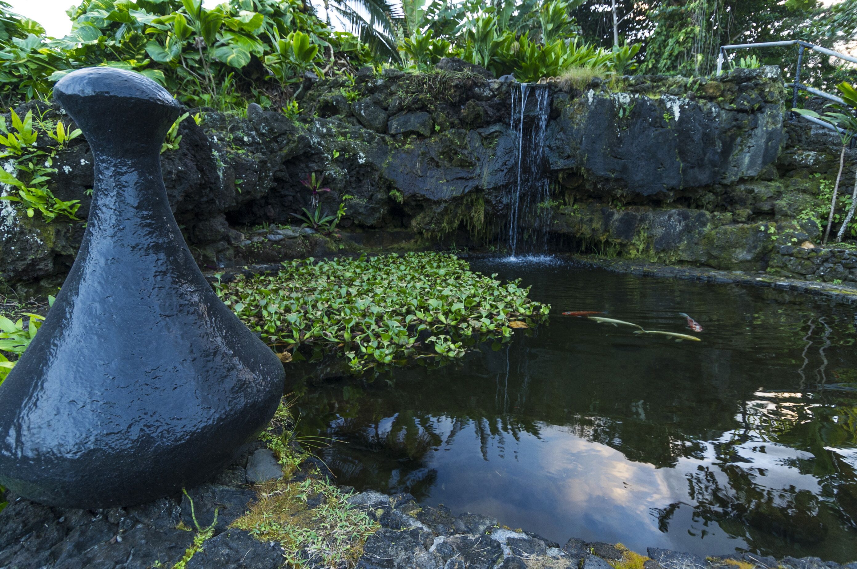 Une sculpture en pierre dans un jardin agrémenté d’un bassin et d’une petite cascade.