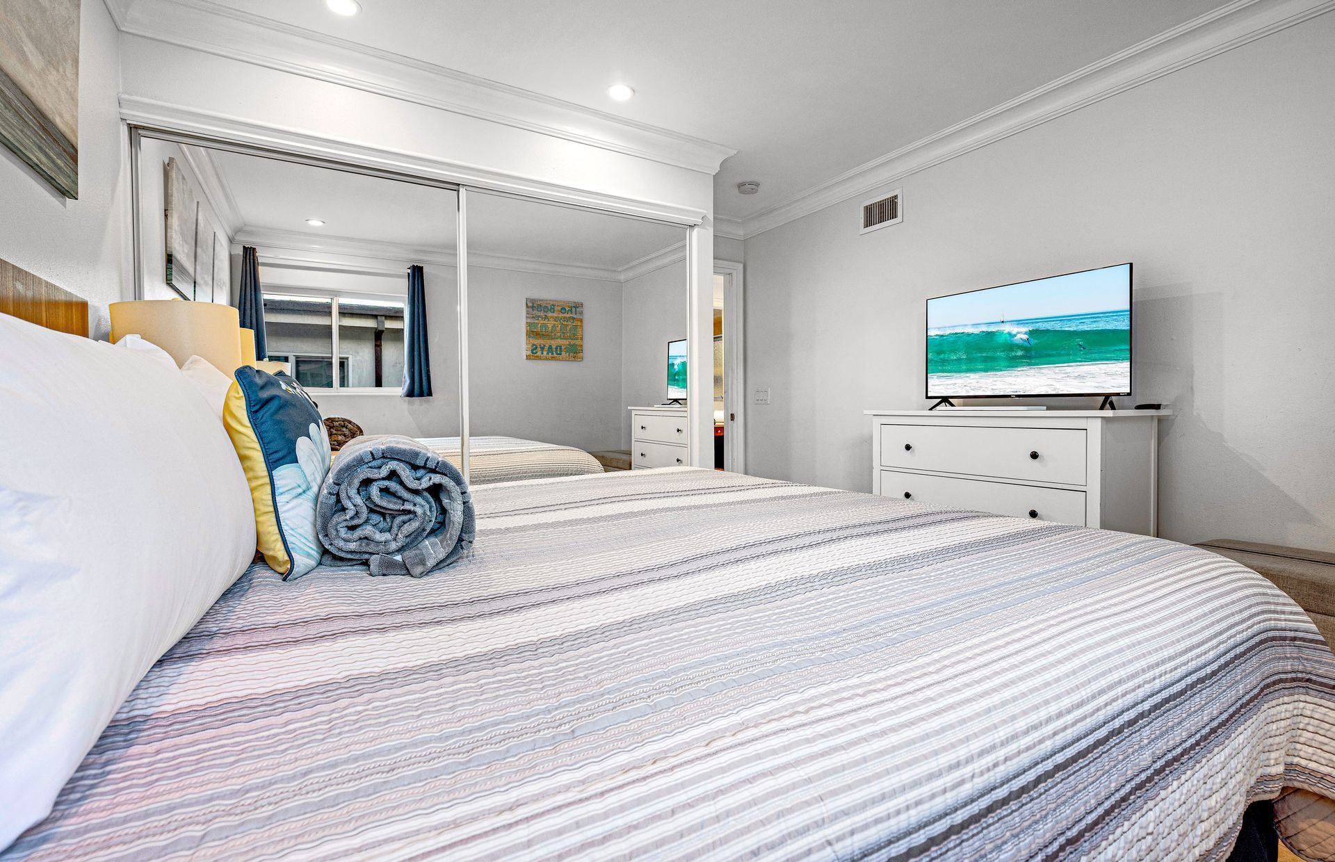 A hotel room with a large bed, a television on a dresser, a mirror, and a view of the ocean.