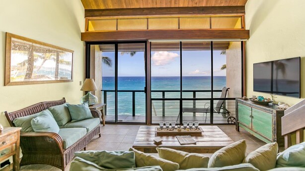 A spacious living room with a large sliding glass door leading to a balcony overlooking the ocean.