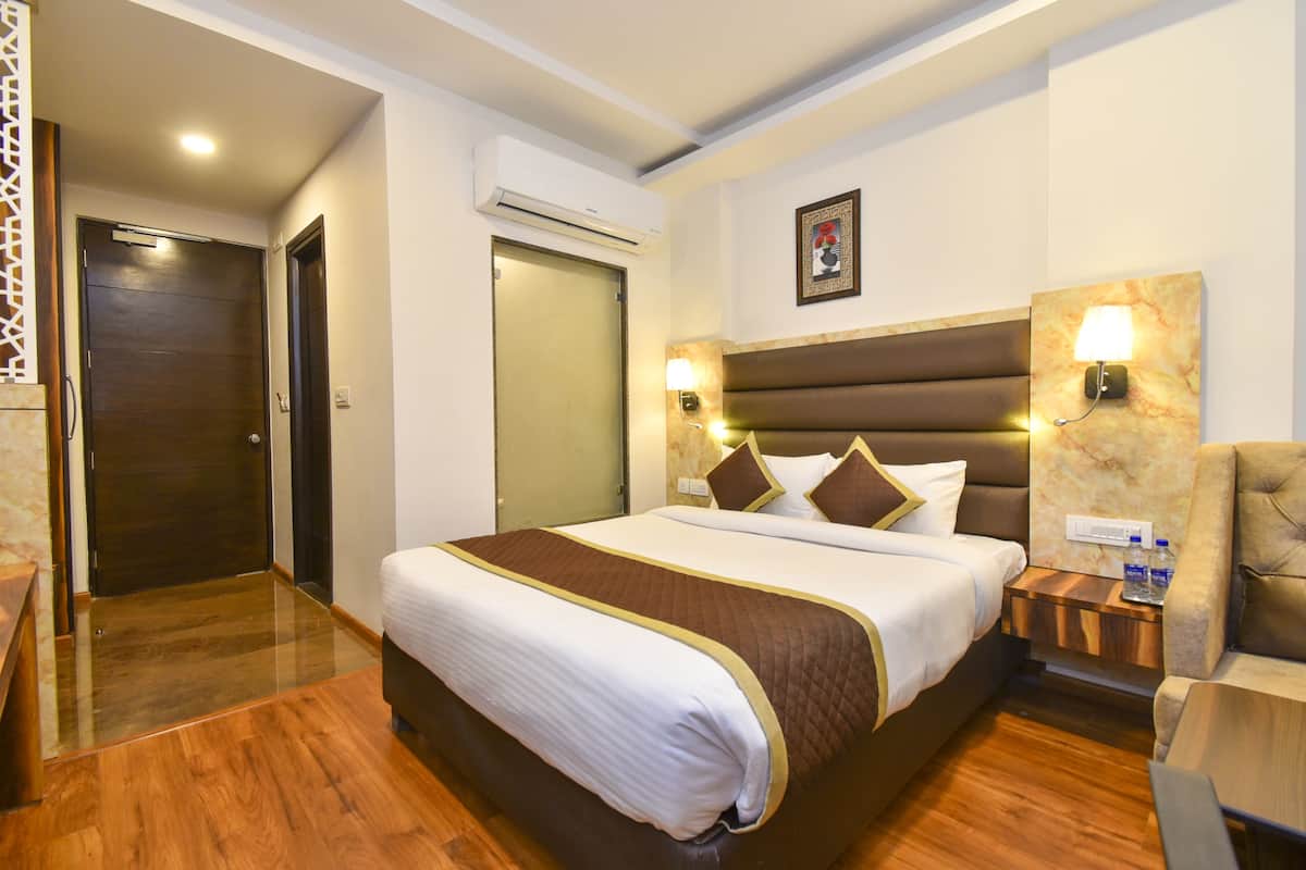 A hotel room with a large bed, a wooden floor, a nightstand with a lamp, and a chair.