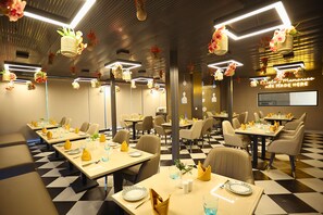 A restaurant with tables set for dining, hanging floral decorations, and a neon sign on the wall. - Hotel Sun City Plaza (Jaipur)