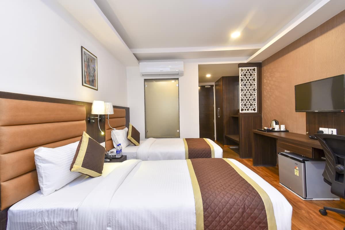A hotel room with two beds, a desk, a television, and an air conditioning unit.