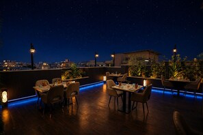 A rooftop restaurant with tables and chairs, city views, and decorative lighting. - Hotel Sun City Plaza (Jaipur)