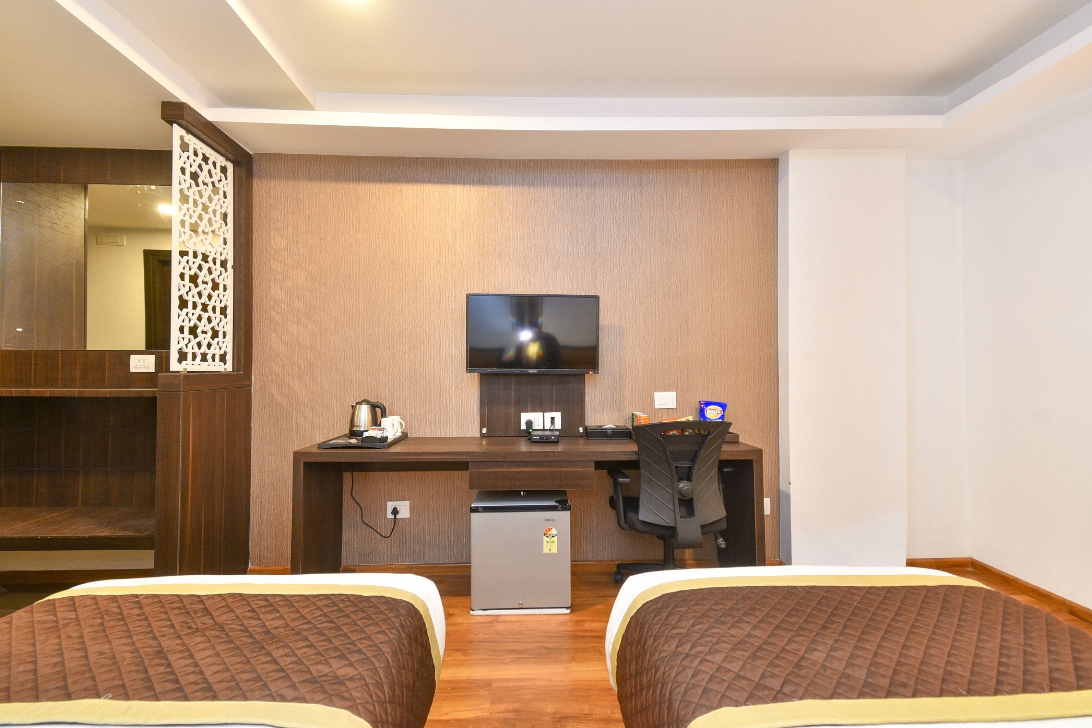 Habitación de hotel con dos camas, un escritorio con computadora y televisor, un refrigerador pequeño y un espejo.