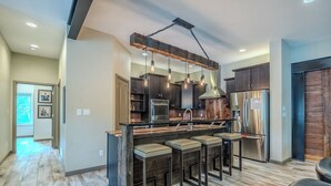 Una cocina moderna con una isla central, taburetes de bar, electrodomésticos de acero inoxidable y un techo de madera rústica.