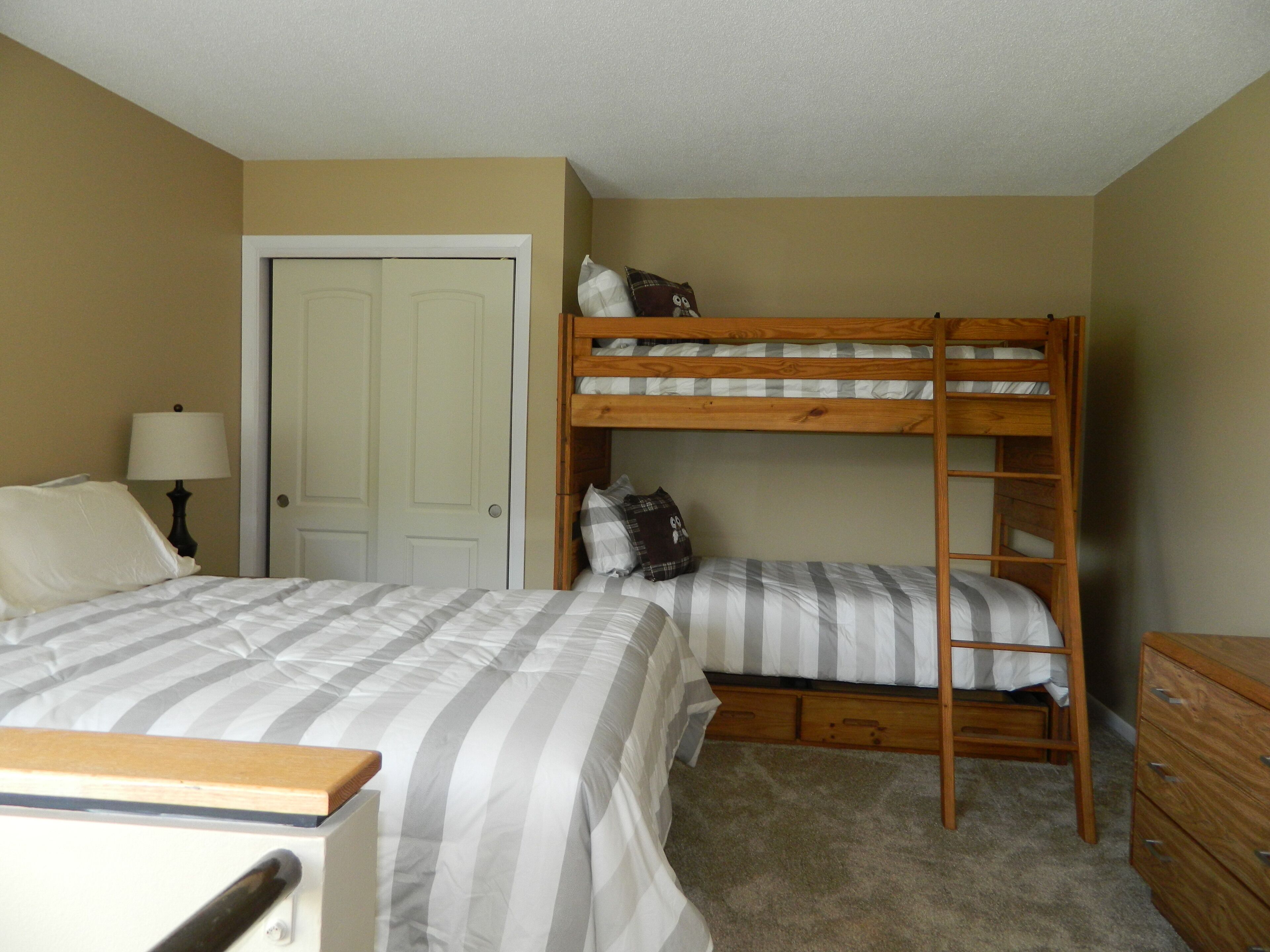 Une chambre avec un lit superposé, un lit simple, une commode et une porte.