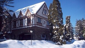 Un bâtiment traditionnel à ossature en bois, avec un toit enneigé, entouré de neige et d’arbres à feuilles persistantes.