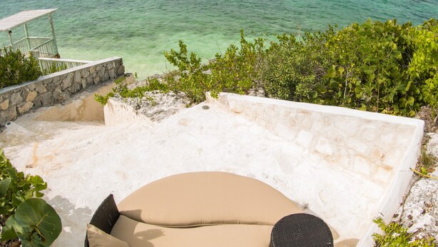 A sun lounger with cushions, overlooking a clear turquoise sea and a white stone wall. - Idyllic Island Getaway, Private Beach Deck & Access (Providenciales)