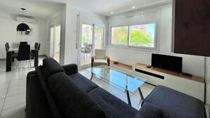 Een moderne woonkamer met een glazen salontafel, zwarte banken en een flatscreen televisie.