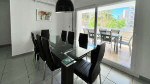 Een moderne eetruimte met een glazen tafel en zwarte stoelen, een hanglamp en een uitzicht op de omgeving door grote schuifdeuren.