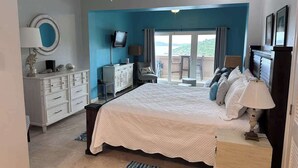 Une chambre avec un grand lit, un ventilateur de plafond, une télévision et un balcon avec vue.