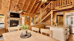 Interior acogedor de una cabaña de troncos con chimenea, escalera de madera y comedor.