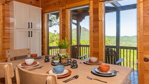 Comedor de una cabaña de madera con una mesa dispuesta para cuatro, un armario blanco y vistas al exterior.