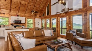 Una cabaña de madera espaciosa con cocina, sala de estar con sofás de cuero y amplios ventanales que ofrecen vistas panorámicas.