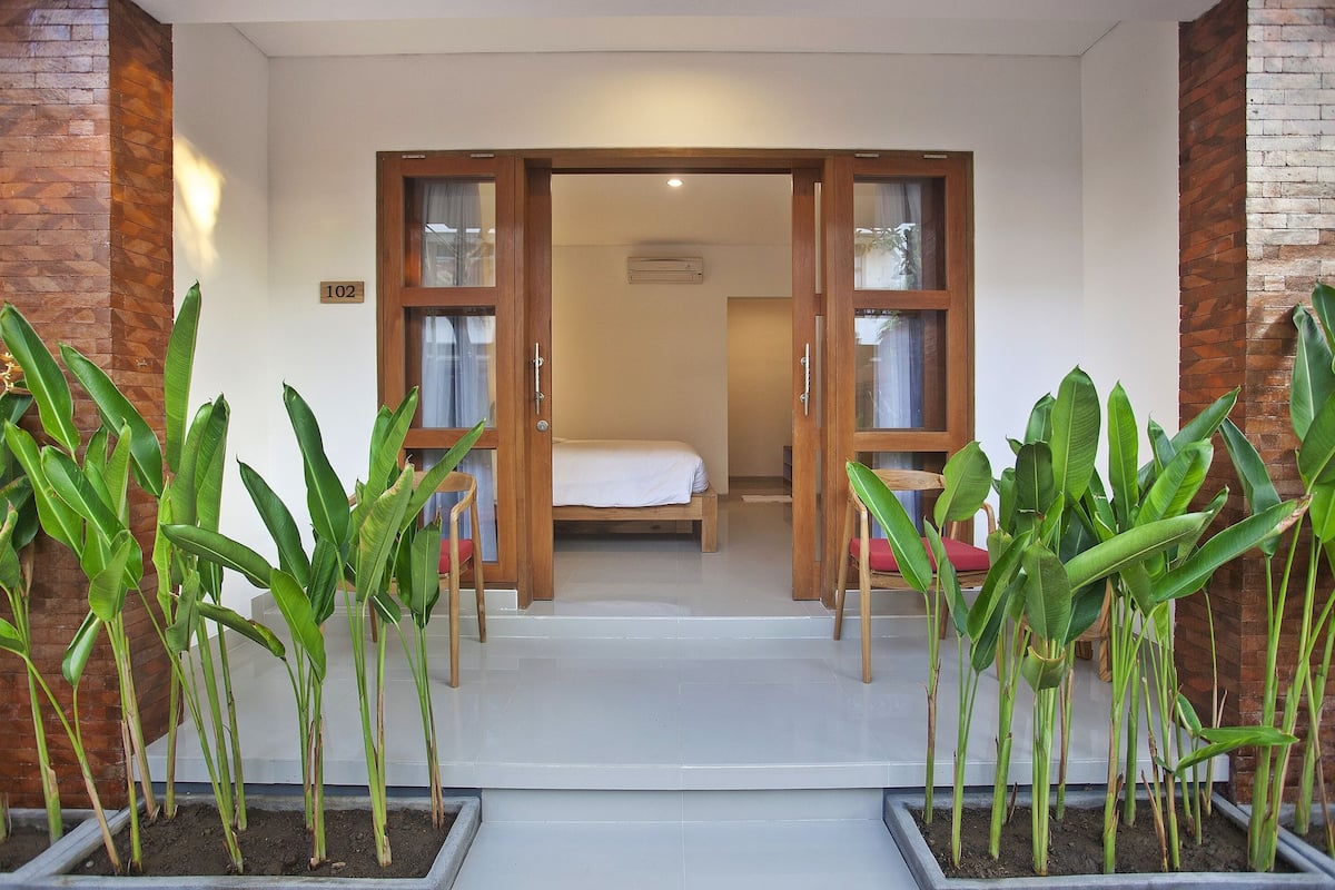A hotel entrance with a bed visible through the open door, surrounded by potted plants.