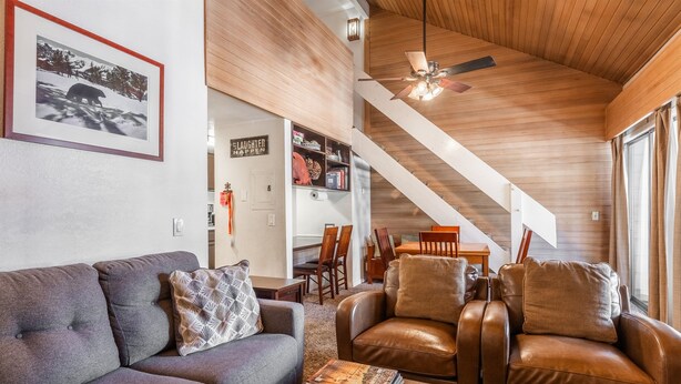 Ein gemütliches Wohnzimmer mit einer Couch, Sesseln und einem Couchtisch. Eine Treppe führt zu einem Essbereich mit Tisch und Stühlen.