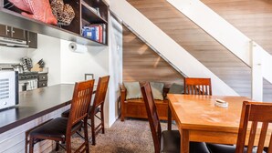 Ein Essbereich mit Holztisch und Stühlen, eine Küche mit Geräte sowie eine Treppe zu einer oberen Ebene.