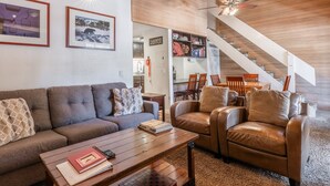 Ein modernes Wohnzimmer mit einer Couch, zwei Sesseln, einem Couchtisch und einer Treppe, die zur Küche führt.