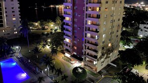 Un hôtel à plusieurs étages doté de balcons, d’une piscine et d’un espace extérieur bien éclairé, agrémenté de palmiers.