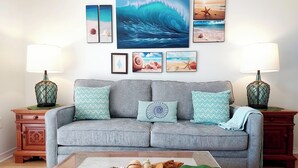 Un salón con un sofá gris, dos mesitas de noche con lámparas y una mesa de centro con un adorno decorativo.