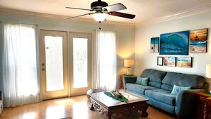Una sala de estar con ventilador de techo, un sofá azul, una mesa de centro y una mesa de comedor con un mantel individual verde.