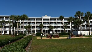 Un hotel de varios pisos con balcones, palmeras y mesas de picnic.