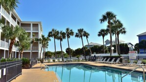 Zona de piscina con sillones de descanso y palmeras, rodeada por un edificio con balcones.