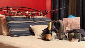 Een bed met gestreepte kussens, een fles champagne, een cadeautas en toiletartikelen.