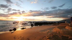 Une scène de plage au coucher du soleil, avec une côte rocheuse et des empreintes de pas dans le sable.
