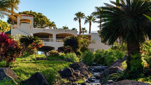 Un complexe hôtelier doté d’une piscine, de palmiers et offrant une vue sur les montagnes.