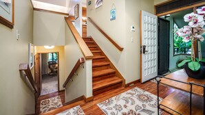 Un escalier en bois avec une rampe, une porte ornée d’un panneau décoratif et un pot contenant une plante orchidée.