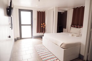Un dormitorio con cama, televisor montado en la pared, ventilador y puerta que da a otra habitación.