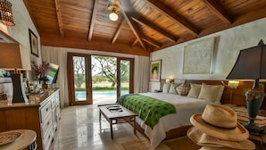 Une chambre spacieuse avec un grand lit, des poutres apparentes en bois au plafond, un bureau et une vue sur l’extérieur.