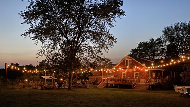 Een landelijk huis met een veranda en lichtjes, omringd door bomen.
