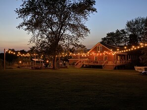Een landelijk huis met een veranda en lichtjes, omringd door bomen.