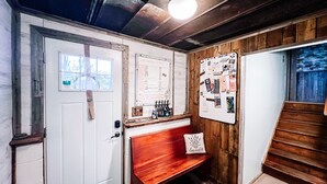 Een kamer met een houten bank, een witte deur, een prikbord en een trap.