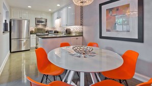 A modern kitchen with white cabinets, stainless steel appliances, and a round table with orange chairs. - Designer Townhouse in the heart of Palm Springs, Convention Center. CITY ID#3867 (Palm Springs)