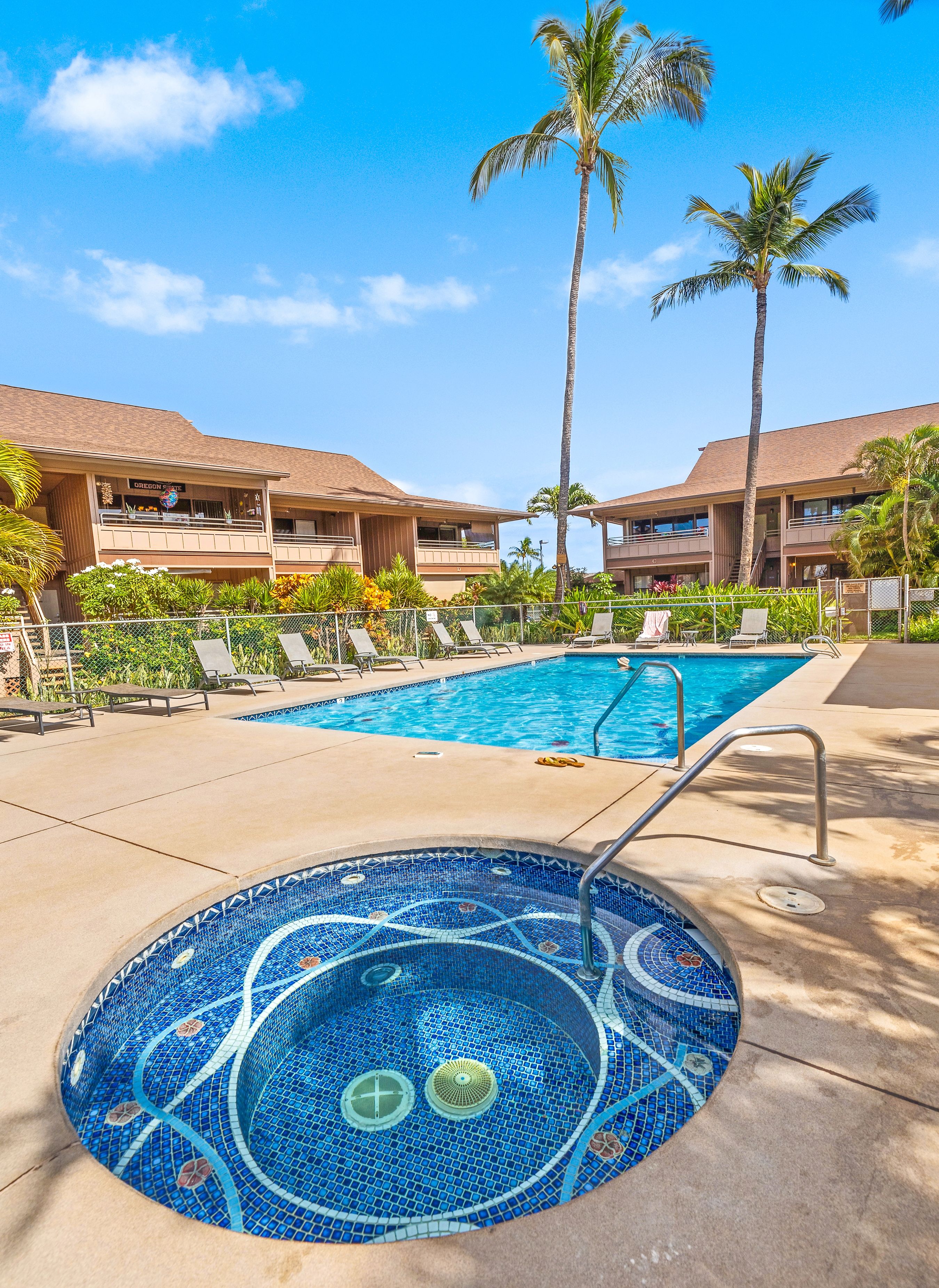 A pool area with lounge chairs, a hot tub, palm trees, and a building with a sign that reads "Oregon".